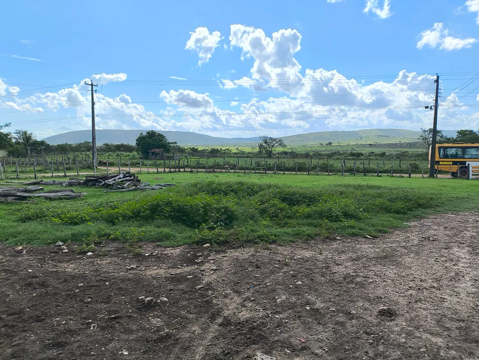 Paisagem rural do povoado Crioulo de Cima, em Lagarto, Sergipe, com campos verdes e morros ao fundo.
