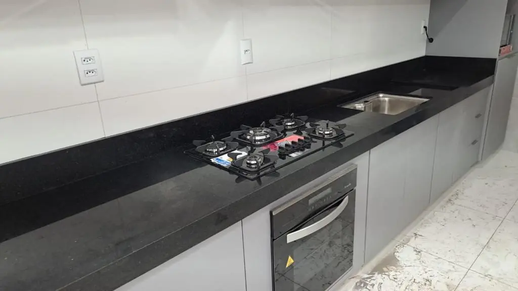 Bancada escura de cozinha com cooktop, pia e forno embutido