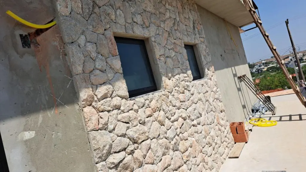 Parede externa revestida com pedras naturais ao redor de duas janelas