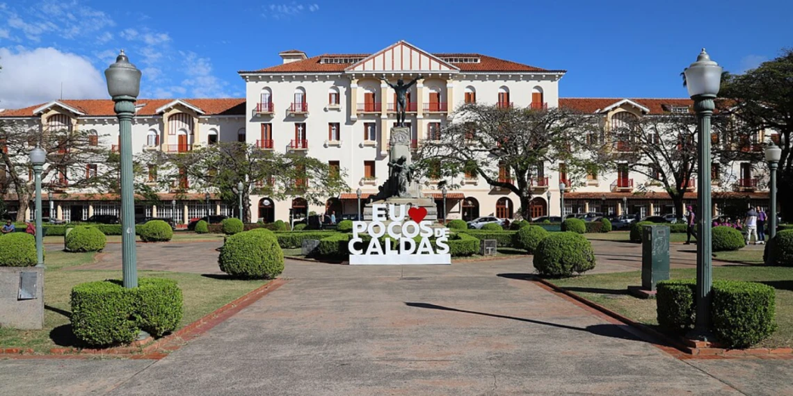 Praça no centro de Poços de Caldas, com jardins, prédio histórico e o letreiro da cidade.
